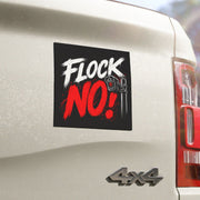 A square black sticker with the text 'FLOCK NO!' in white and red brush-style lettering, shown applied to the rear side of a white vehicle. The sticker includes a small wrench graphic and is photographed outdoors with a blurred background.