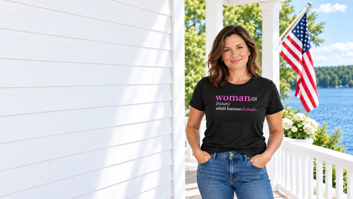 Woman wearing the black Definition of a Woman T-shirt beside an American mountain lake